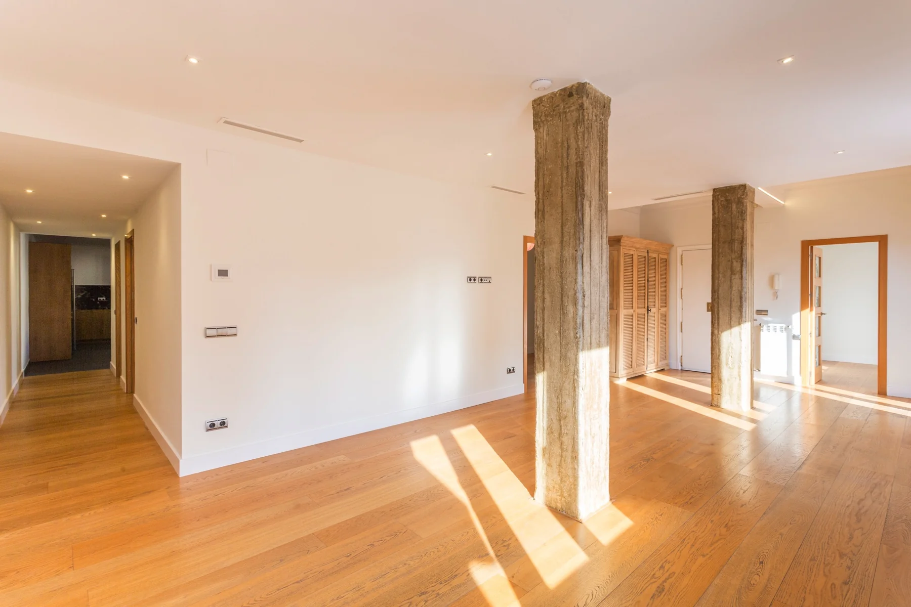 Salón luminoso con suelo de madera y pilares de hormigón