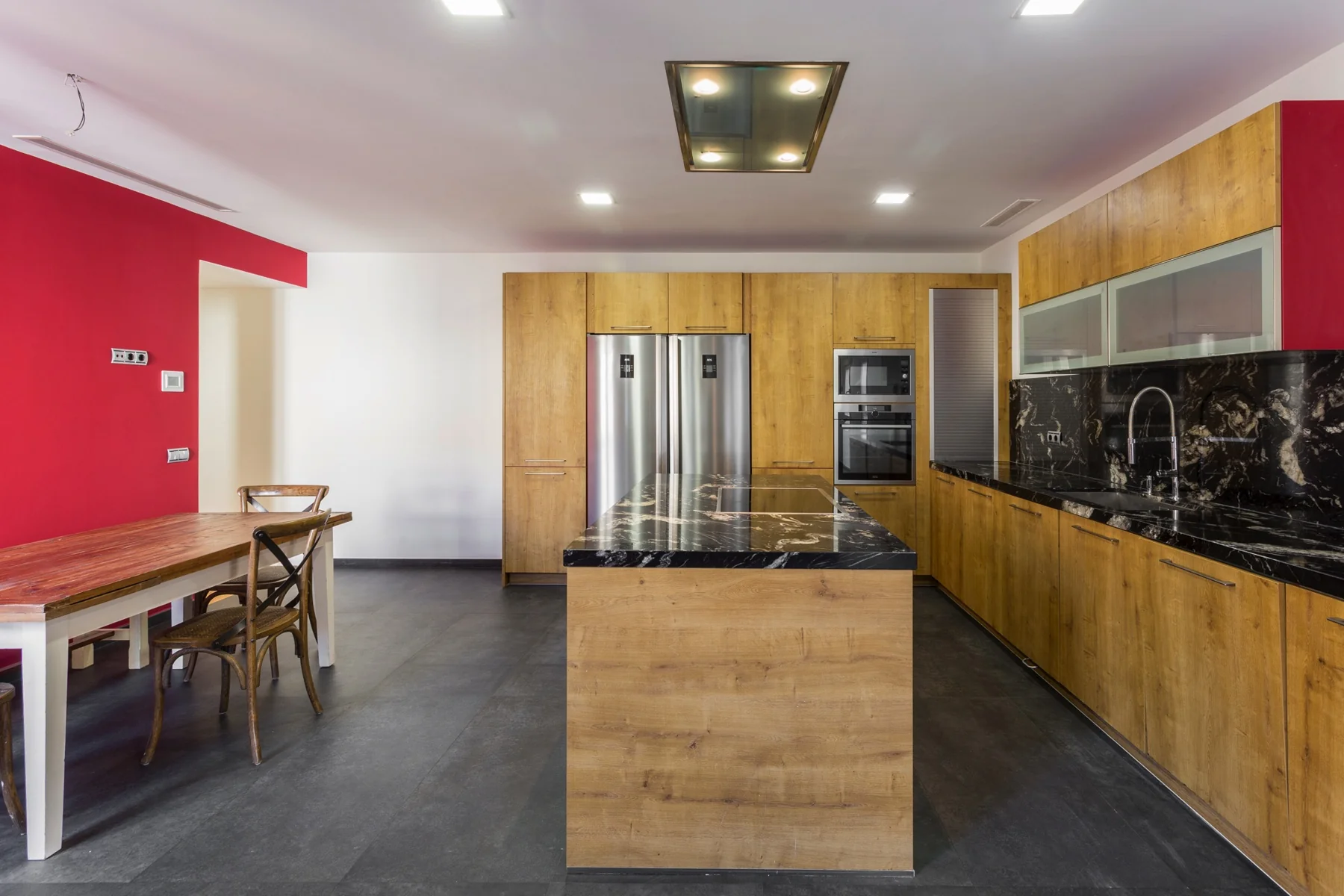 Cocina de madera con una isla central y pared roja