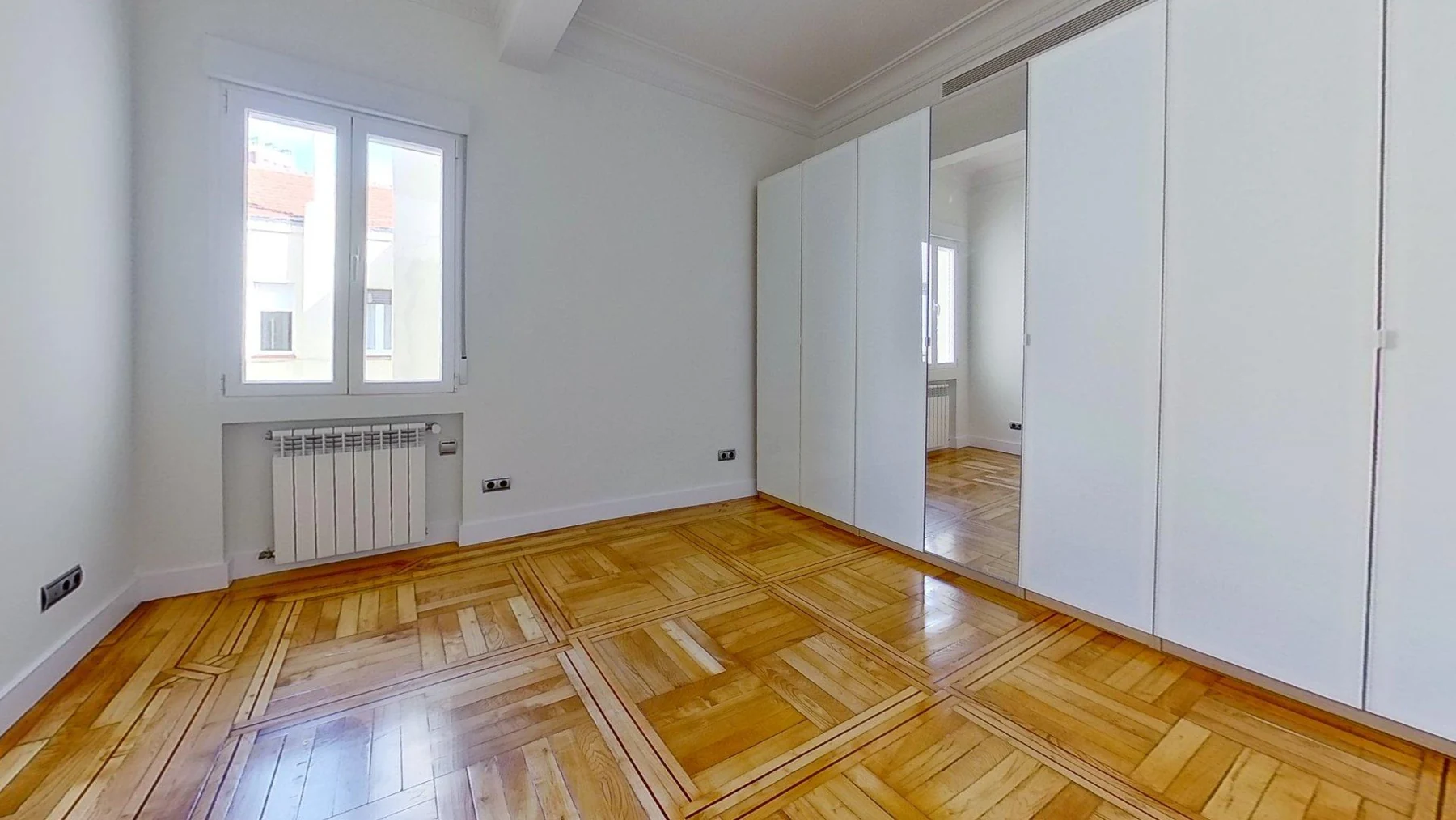 Habitación con armario blanco, ventana y suelo de parqué